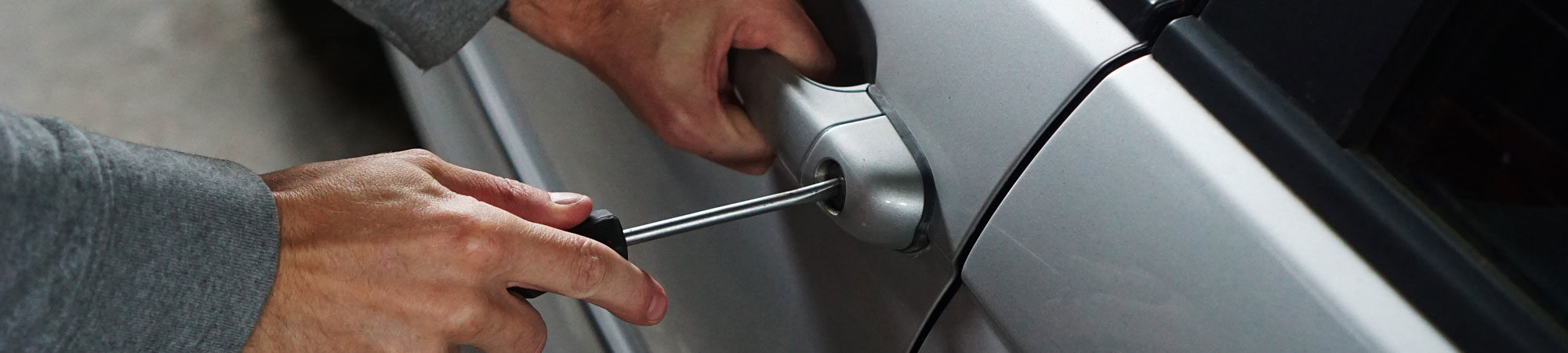 A close-up of a person's hands using a screwdriver to remove a screw from a car door hinge.