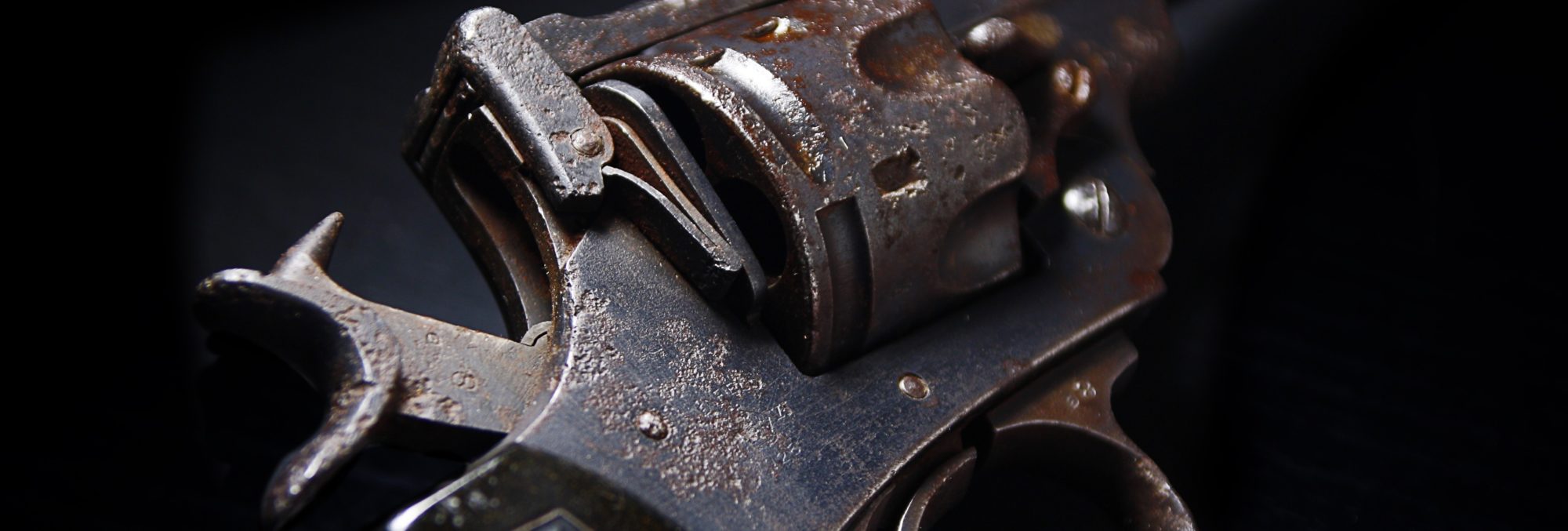 Close-up of an old, rusted revolver on a dark background, highlighting the detailed texture and mechanical parts of the firearm.