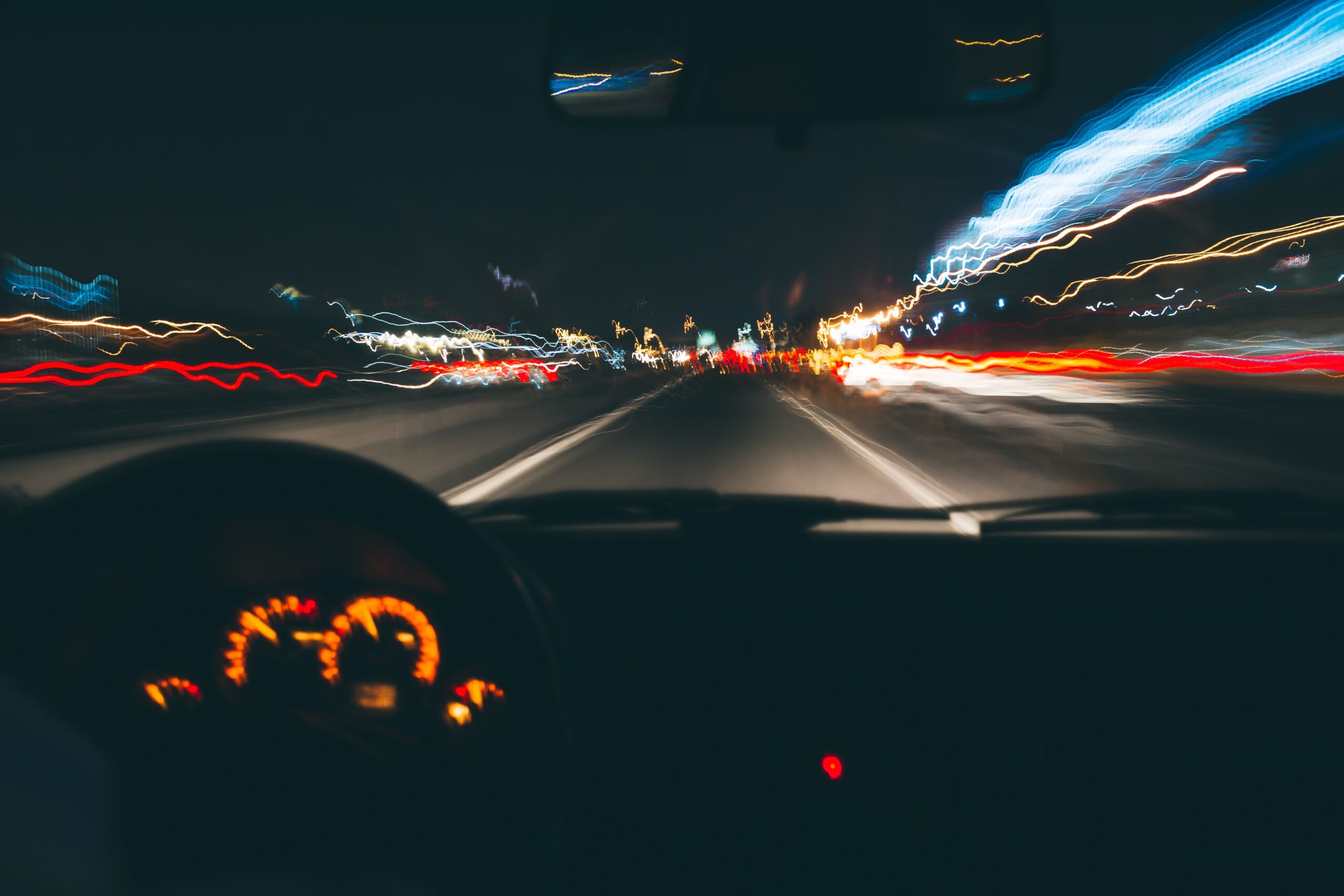 A night scene of a road in New Jersey from a driver's perspective, with blurred lights streaking past and a dashboard visible in the foreground, creating a dynamic sense of motion.