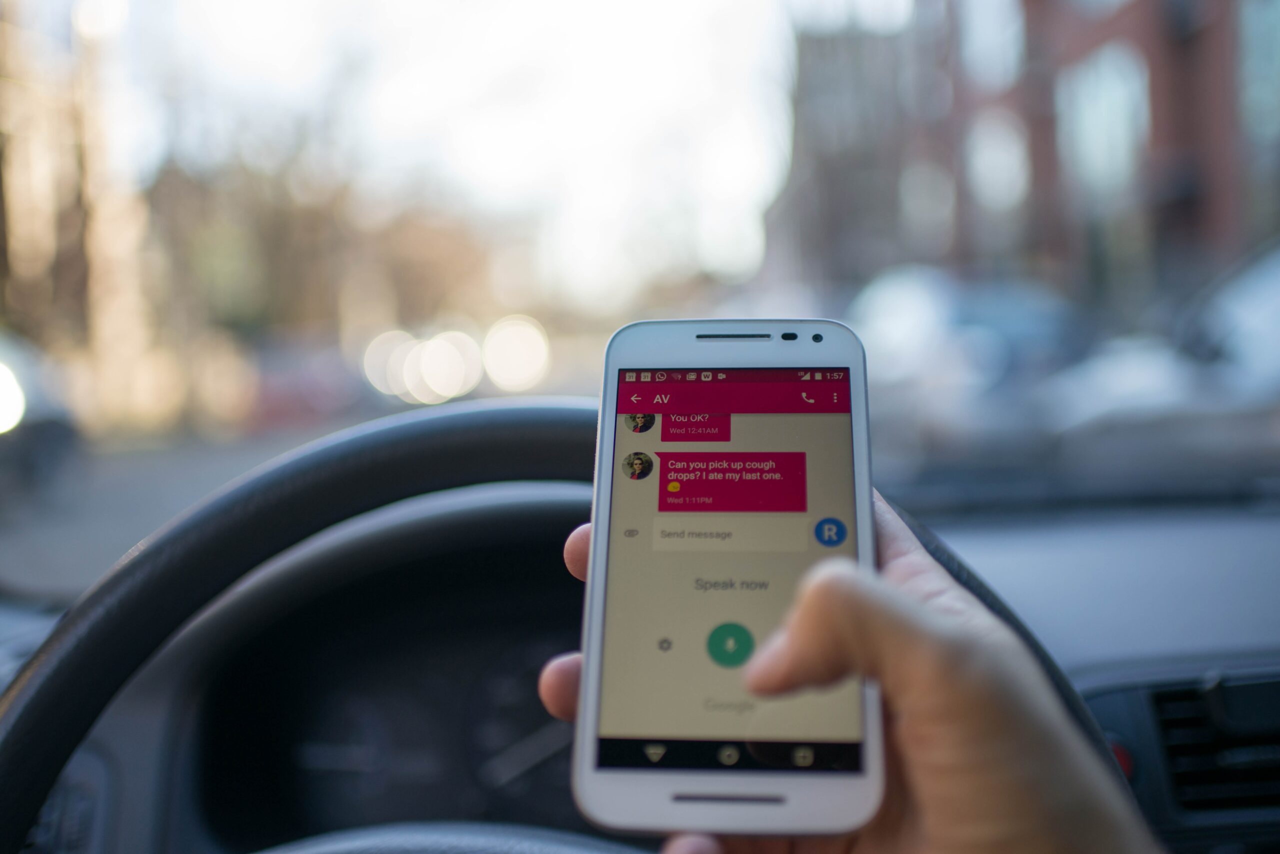 A person holding a cell phone displaying a text message conversation, with a blur of a steering wheel and street in the background, emphasizing unsafe driving behavior indicative of a New Jersey cell phone violation.