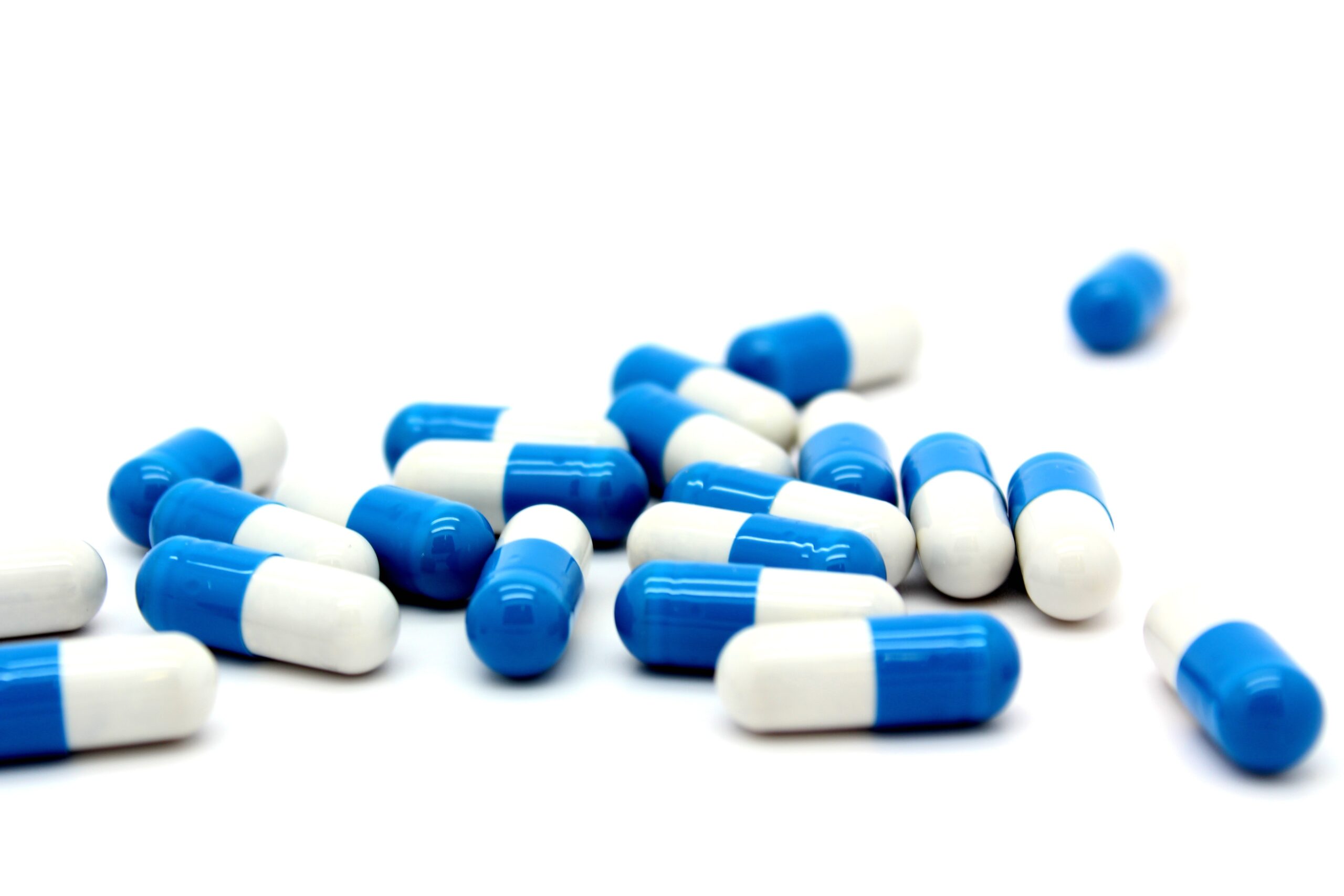 A collection of blue and white capsules, representing consequences of Drug DWI, scattered on a white background.