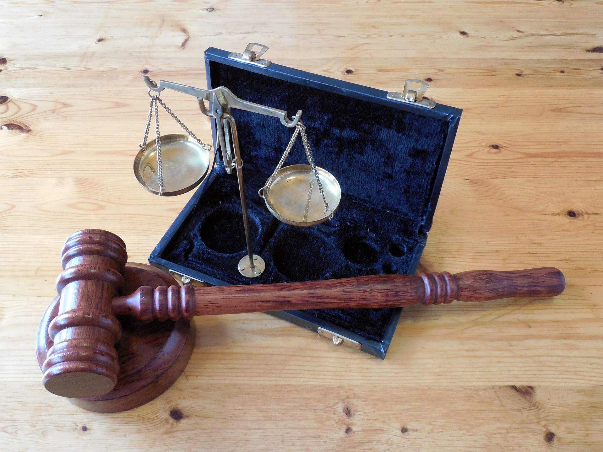 A wooden gavel lies next to an open, small briefcase displaying a set of brass scales on a wooden table, symbolizing law and justice in New Jersey.