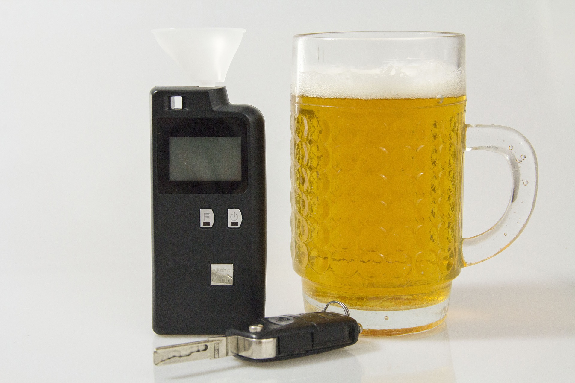 A breathalyzer device next to a full mug of beer and car keys on a white background, representing the connection between alcohol consumption and driving. This setup highlights the importance of breathalyzer test validity in ensuring