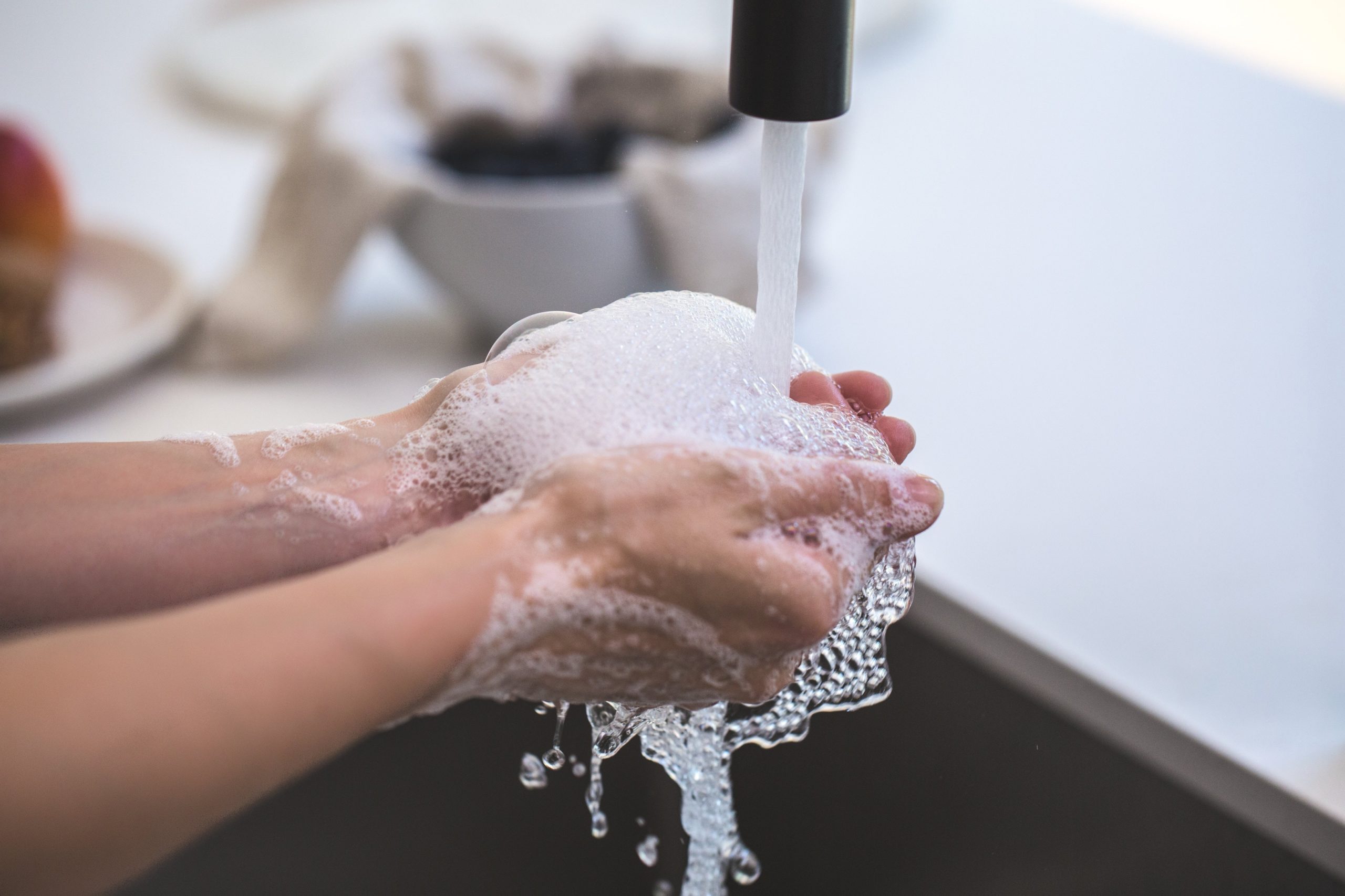 A person thoroughly washing hands with soap under a running faucet, with lather covering both hands, emphasizing cleanliness as a preventive measure against coronavirus disease symptoms.
