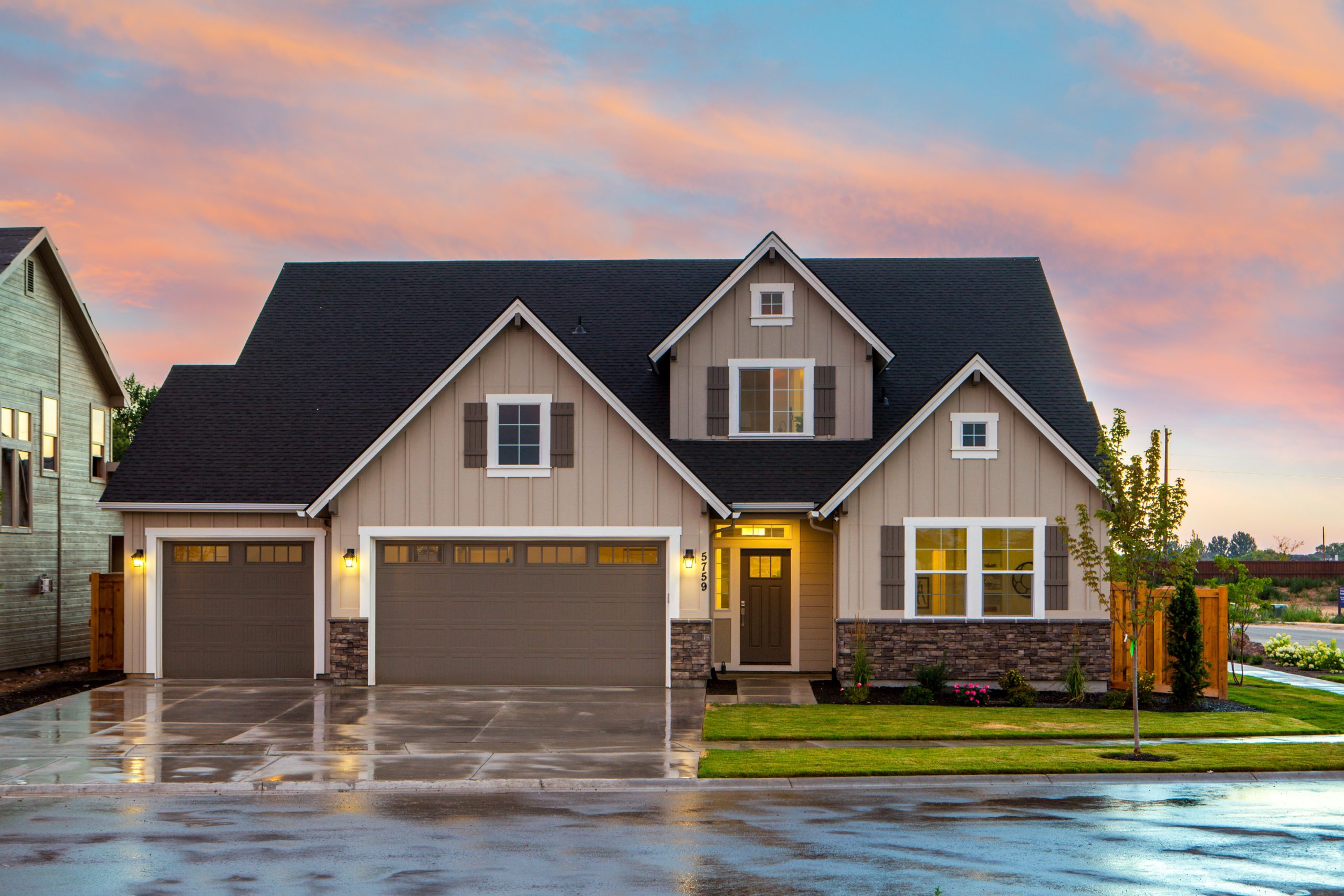 A large two-story suburban home in New Jersey with a beige and brown exterior, featuring a double garage and a landscaped front yard, set against a vibrant sunset sky.