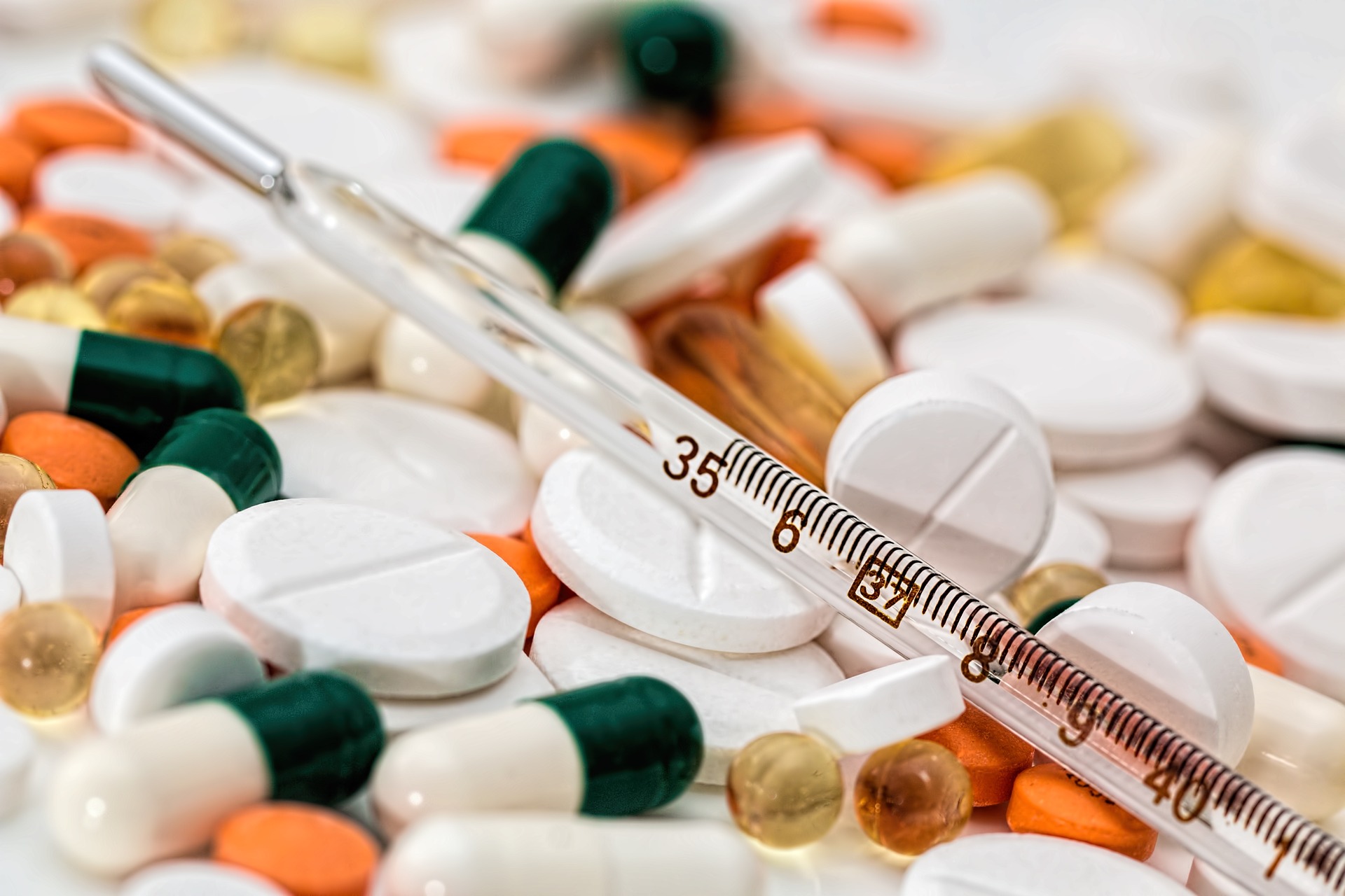 A close-up image of a variety of drugged medications including pills, capsules, and a glass thermometer, showcasing a mix of shapes and colors.