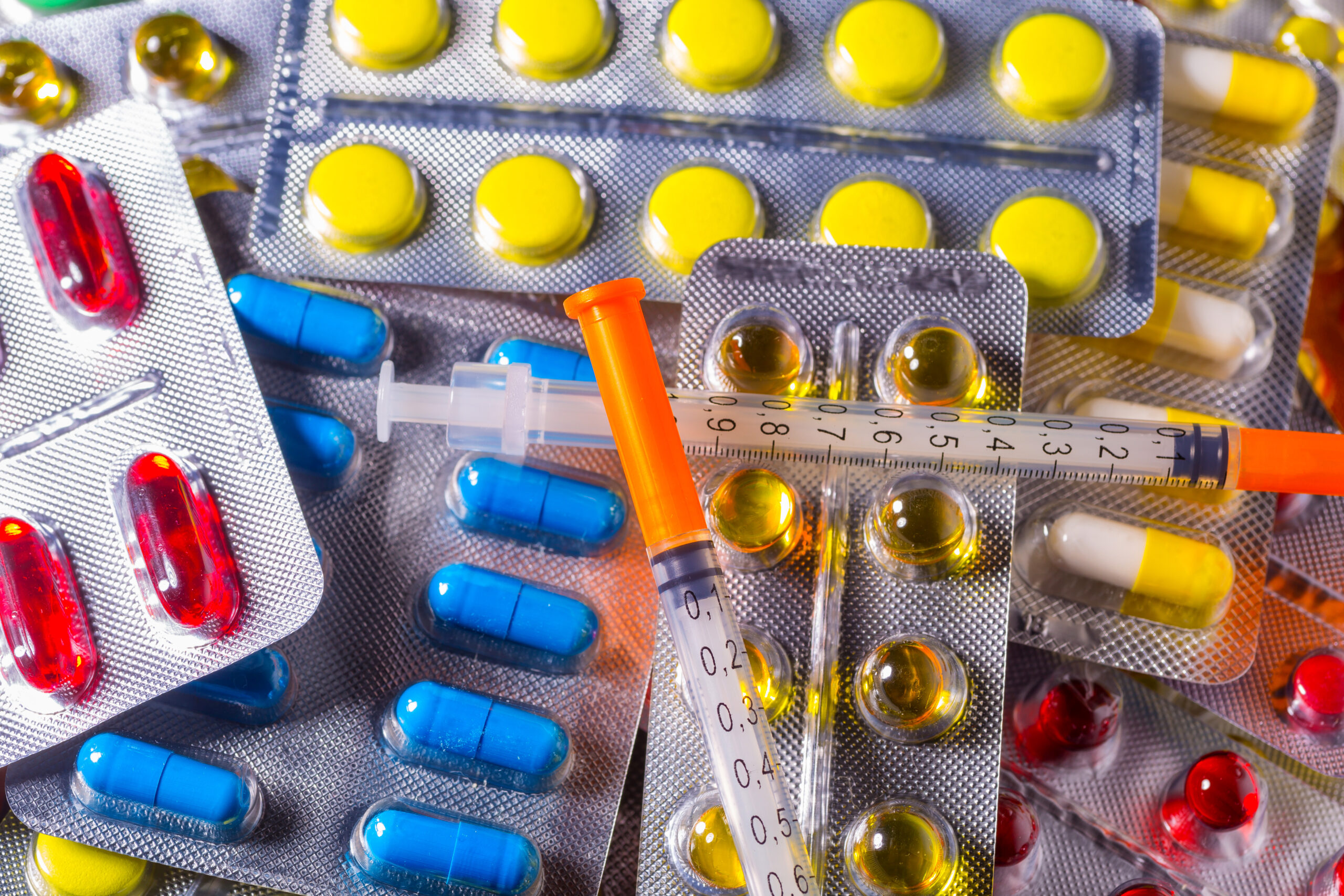 Assorted pharmaceutical drugs including capsules, pills in blister packs, and a syringe, showcasing drug distribution and a thermometer.