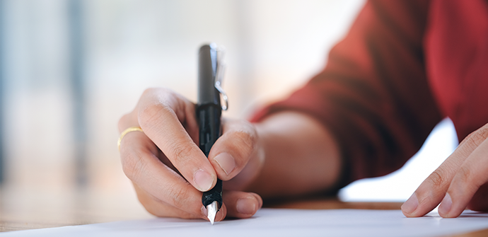 A close-up image of a Bergen County Criminal Defense Attorney's hands holding a black pen and writing on a piece of paper, with a soft-focus background.