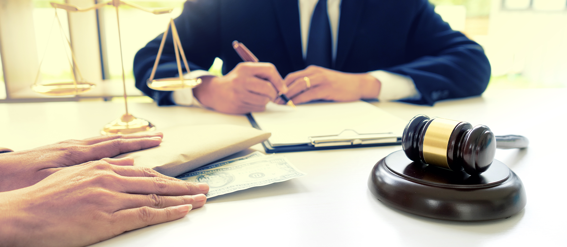 A lawyer in a suit and a client signing documents next to a gavel and money on a desk, symbolizing a legal financial agreement.