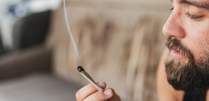 Close-up of a bearded man smoking a joint with a focused expression, indoors with a blurred background, possibly needing the expertise of a Bergen County criminal defense attorney.
