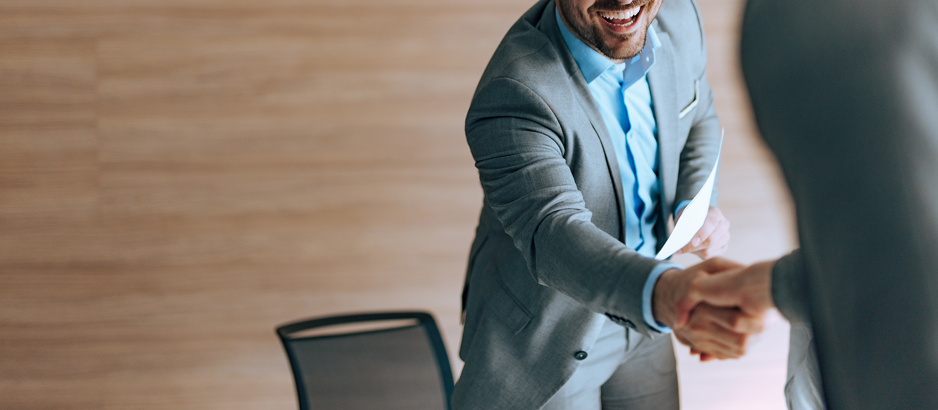 Two business professionals, a man and a woman, joyfully shaking hands in an office setting, emphasizing a successful engagement or agreement.