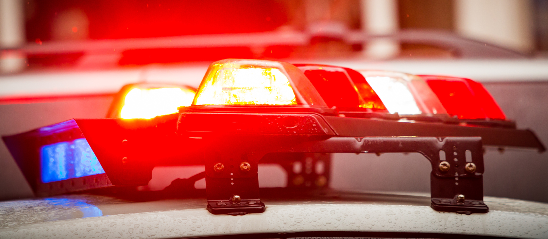 Close-up of a police car's roof with a flashing red and blue light bar, parked outdoors, indicating urgent law enforcement activity.