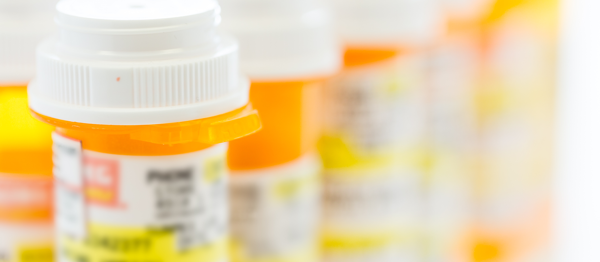 Close-up image of orange and white prescription medicine bottles, with focus on the front bottle cap while rest are blurred in the background. Labels are partially visible but details are obscured, demonstrating an issue relevant to