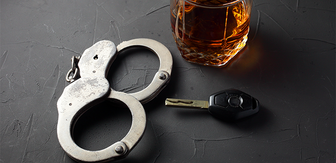 A glass of whiskey, handcuffs, and a car key on a textured black surface, symbolizing the dangers of drinking and driving, potentially requiring the services of a Bergen County Criminal Defense Attorney.